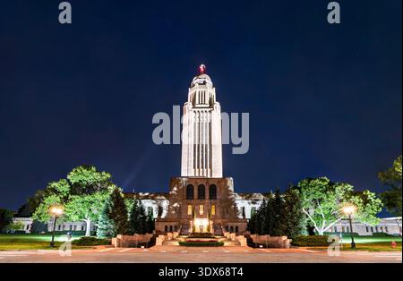 Nebraska State Capitol in Lincoln bei Nacht. Der historische Art déco-Wolkenkratzer verfügt über einen Kalksteinturm und eine goldene Kuppel, die vor einem dunkelblauen Himmel beleuchtet wird Stockfoto