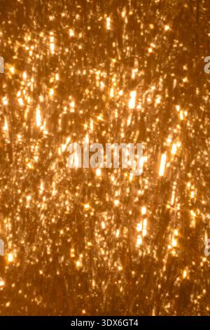 Ein strahlender abstrakter Hintergrund mit leuchtenden Bokeh-Lichtern und glitzernder Glitzerstruktur sorgt für ein warmes, festliches und bezauberndes visuelles Ambiente Stockfoto