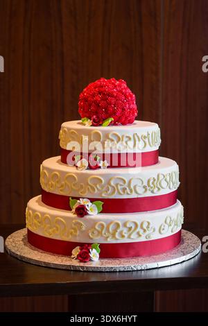 Eleganter dreistöckiger, weißer und roter Kuchen mit Blumen, Bändern und Glasur. Stockfoto