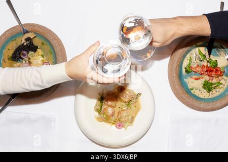 Ein Blick von oben auf ein Gourmet-Dining-Erlebnis mit eleganten Gerichten auf Keramikplatten und zwei Personen, die mit Weingläsern über einem wunderschönen Stockfoto
