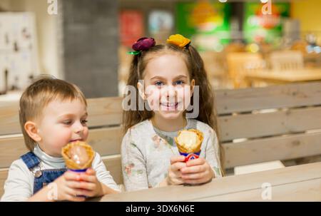 Zwei Kinder teilen sich Eisbecher, während sie an einem Holztisch drinnen im Familienunterhaltungs-Center sitzen. Stockfoto