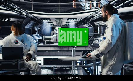 Astronauten fliegen zusammen in einem Raumschiff, schauen auf einen isolierten Bildschirm und sammeln Proben für die Untersuchung. Wissenschaftler benutzen Chroma Key Display, bevor sie auf dem roten Planeten landen Stockfoto