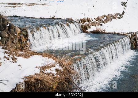 Zweistufiger Wasserfall am Yokoyugawa River mit schneebedeckten Ufern in Shibu Onsen Stockfoto