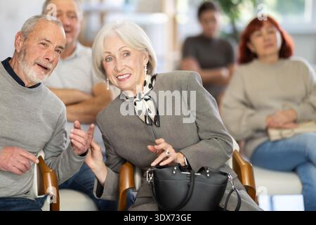 Kommunikativer älterer Mann und Frau im Gespräch, während er in einer fokussierten Gruppe von Menschen sitzt, die einen Vortrag im Konferenzsaal hören Stockfoto