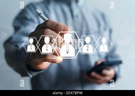 Nahaufnahme eines Geschäftsmanns, der auf einer virtuellen Netzwerkschnittstelle ein Kandidatensymbol auswählt, während er das Smartphone hält. Dies symbolisiert Personalrekrutierung und Talentauswahl Stockfoto