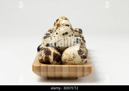 Wachteleier sind ordentlich auf einem Holzteller aufgereiht. Die Eier haben ein einzigartiges gesprenkeltes Muster. Stockfoto