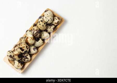 Ein Holztablett hält mehrere Wachteleier in verschiedenen Farben und Mustern. Die Eier sind ordentlich auf einer glatten weißen Oberfläche angeordnet. Stockfoto