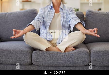 Ältere achtsame gesunde reife Frau, die in Lotusposition sitzt und Meditation zu Hause praktiziert, ruhige ältere Stockfoto