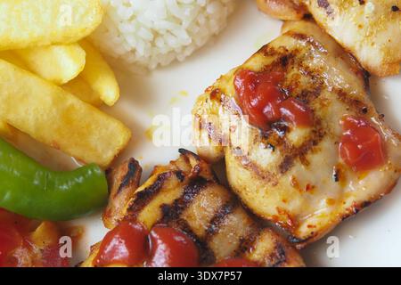 Gegrilltes Hühnchen mit Reis und Pommes frites auf einem Teller Stockfoto