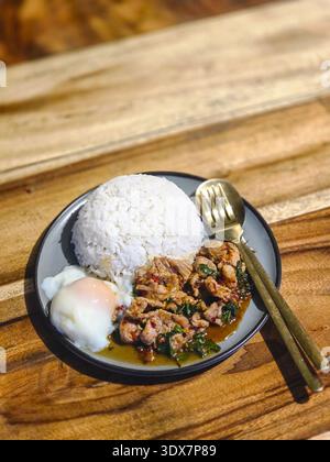 Köstlicher Teller mit Pad Kra Pao, scharfem Thai-Basilikum-Rührbraten mit Huhn und Reis. Herzhafte und beliebte asiatische Küche, komplette Mahlzeit mit pochiertem Ei Stockfoto