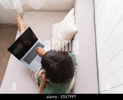 Ältere Frau, die in gemütlicher Atmosphäre mit entspanntem Komfort am Laptop arbeitet Stockfoto