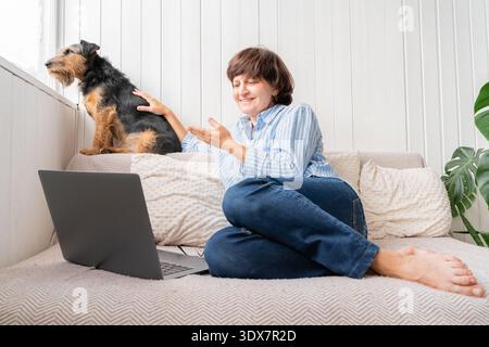 Kaukasische Erwachsene Frauen Videoanrufe mit Laptop, sitzen auf Sofa mit Hund, zwanglose Inneneinrichtung Stockfoto