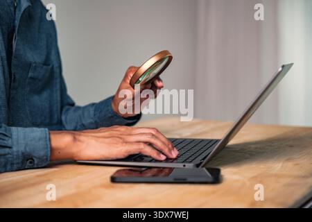 Ein Mann in einer zielgerichteten geschäftlichen Pose hält eine Lupe über einem Laptop, eine Handgeste und eine intensive Pose, die Konzepte wie Entdeckung und tiefe d repräsentieren Stockfoto
