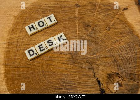 Zwei Scrabble-Fliesen schreiben die Worte Hot Desk auf einer runden Holzfläche. Diese Szene feiert den National Scrabble Day auf einfache und fesselnde Weise. Stockfoto