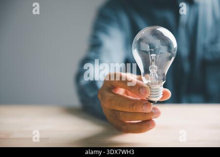 Nahaufnahme einer Hand, die eine Glühbirne vor einem verschwommenen Hintergrund hält und Ideen und Innovation symbolisiert. Stockfoto