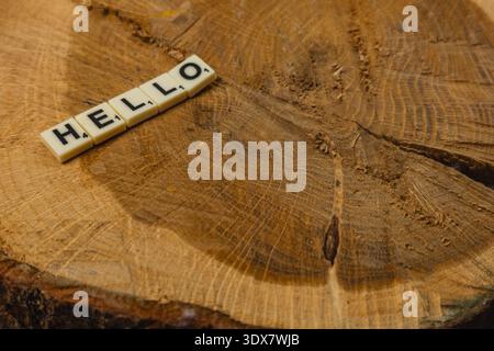 Die Leute spielen gerne Scrabble am National Scrabble Day. Ein Satz Buchstaben schreibt das Wort „Hallo“ auf einem runden Holzstück. Das Spiel bringt Freunde und Stockfoto