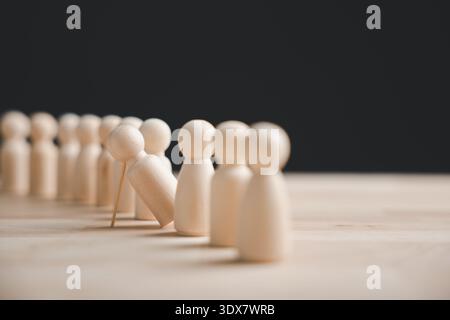 Eine Reihe von Holzfiguren steht auf einem Tisch, eine fällt um. Die Figuren sind außer Fokus, bis auf die fallende Figur, die im Fokus ist. Stockfoto