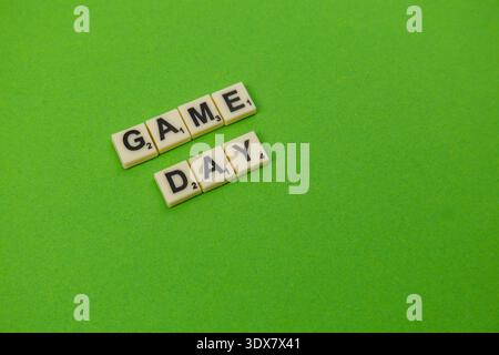 Am National Scrabble Day stehen hölzerne Buchstabenziegel auf einer hellgrünen Oberfläche für den Spieltag. Die Spieler genießen eine lustige Zeit, die sich auf Worte und Strategie konzentriert. Stockfoto