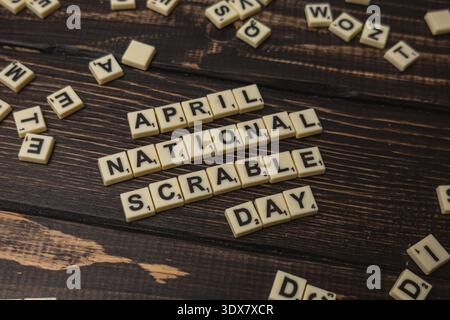 Auf einem Holztisch verstreute Buchstaben geben den National Scrabble Day an, den die Spieler genießen können. Die Aktivität findet im April statt und konzentriert sich auf Wortspiele und Spaß Stockfoto