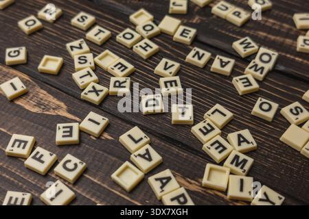 Scrabble Fliesen sind auf einem Holztisch zum National Scrabble Day verstreut. Freunde treffen sich, um ein lustiges Wortspiel zu genießen und eac herauszufordern Stockfoto
