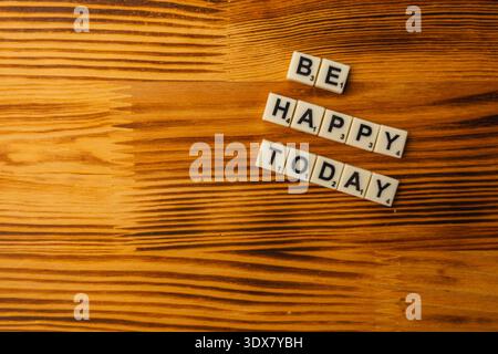 Die Leute versammeln sich auf einem Holztisch, um Scrabble zu genießen. Buchstabensteine geben eine freundliche Nachricht an, die die Veranstaltung am National Scrabble Day mit Freude erfüllt. Stockfoto