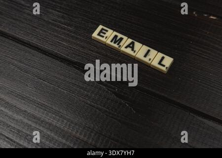 Die Spieler genießen den National Scrabble Day, indem sie das Wort E-MAIL mit Buchstabensteinen auf einer dunklen Holzoberfläche Formen. Freunde kommen zusammen, um sich gegenseitig in wo herauszufordern Stockfoto