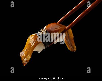 Nahaufnahme von Stäbchen, die Aal Nigiri Sushi mit süßer Sauce auf schwarzem Hintergrund halten Stockfoto