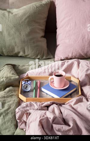 Frühstück im Bett, Holztablett mit Kaffeetasse, Buch und Wecker. Gemütliche Atmosphäre am Morgen. Entspannendes, faules Wochenende. Stockfoto