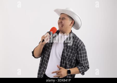 Glücklicher Mann mit weißem Hut, der im Studio mit Mikrofon singt Stockfoto
