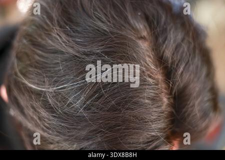 Nahaufnahme von oben auf eine Person mit grauem, dunklem Haar in der Mitte. Dieser natürliche Alterungsprozess zeigt erste Anzeichen von Silbersträngen auf der Kopfhaut und Stockfoto