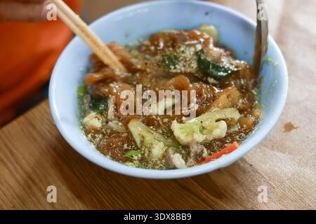 Nahaufnahme von köstlichen asiatischen Nudelgerichten in der Schüssel. Person, die mit Essstäbchen isst, genießt leckeres Mittagessen mit herzhafter Sauce und frischem Gemüse Stockfoto