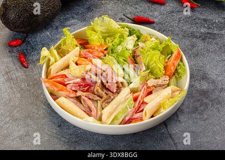 Appetitlicher Nudelsalat mit Thunfisch und Gemüse in einer cremigen Sauce. Die Top-Down-Ansicht auf dunklem Hintergrund hebt frische rote, grüne und beige Farben hervor. P Stockfoto