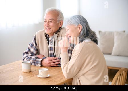Lachendes Seniorenpaar, das Kaffee am Esstisch trinkt Stockfoto