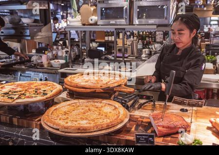 Phuket Thailand 29 11 2025: Ein Schaufenster mit mehreren Arten von frisch gebackener Pizza auf Holzständern und dem Prozess des Schneidens von gebackenem Fleisch, wahrscheinlich hone Stockfoto