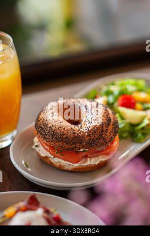 Gerösteter Mohnbagel gefüllt mit Frischkäse und Räucherlachs, serviert mit einem frischen grünen Salat aus Salat, Kirschtomaten und Gurke. Stockfoto