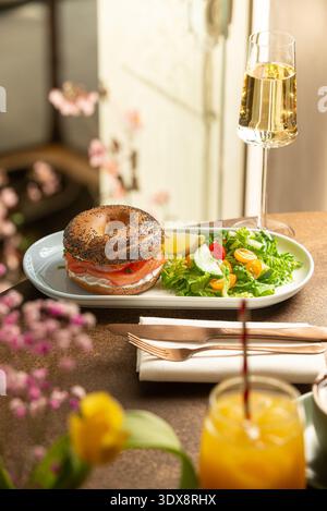 Gerösteter Mohnbagel gefüllt mit Frischkäse und Räucherlachs, serviert mit einem frischen grünen Salat aus Salat, Kirschtomaten und Gurke. Stockfoto