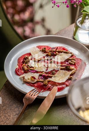 Dünn geschnittenes rohes Rindfleisch-Carpaccio, elegant überzogen mit geschmortem Parmesankäse, cremiger Senfsauce, Kapern, Pinienkernen und frischem Mikrogrün. Stockfoto
