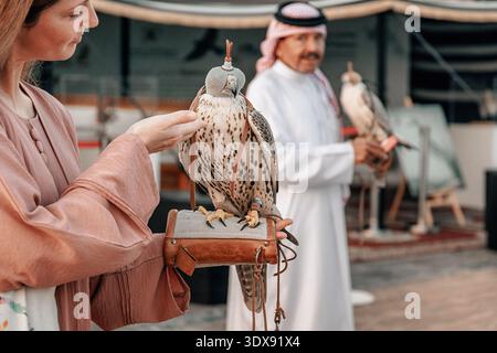 1. Dezember 2025, Doha, Katar: Frau, die bei einer Kulturausstellung einen Falken mit Kapuze anfasst, der auf ihrer Hand thront Stockfoto