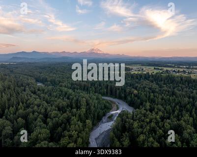 Aus der Vogelperspektive eines majestätischen Flusses, der sich durch einen dichten, grünen Wald schlängelt, zum entfernten, schneebedeckten Gipfel des Mount Rainier, Washington, United Sta Stockfoto