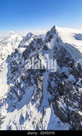 Aus der Vogelperspektive auf schneebedeckte Berge, die den hellblauen Himmel durchdringen, ihre zerklüfteten Gipfel und vereisten Hänge, die einen atemberaubenden Kontrast schaffen, Valfurva, Provinz Stockfoto