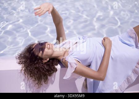 Frau, die ihre empfindliche Gesichtshaut vor schädlichem UV-Sonnenlicht schützt, Sonnenschutz, Entspannen, Pool, Urlaub, Sommer, Liegen, chillen, Erholung, Bequemlichkeit Stockfoto