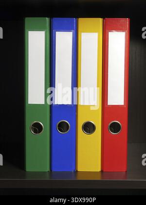 Vier leere Ordner in den Farben Grün, Blau, Gelb und Rot im schwarzen Schrank Stockfoto