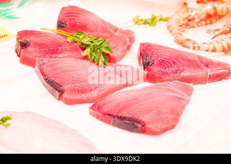 Nahaufnahme von frischen, rohen Thunfischsteaks mit tiefrotem Fleisch und dunklen Kanten. Die Steaks werden mit einem Zweig Petersilie garniert und auf weißem Papier präsentiert Stockfoto