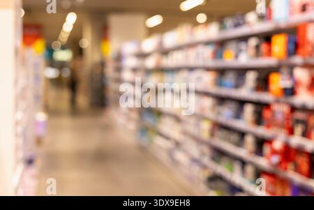 Verschwommene Perspektive auf hell beleuchtete Supermarktgänge mit farbenfrohen Produkten in Regalen, die einen klaren abstrakten Einkaufshintergrund für Einzelhandelskontrakte schaffen Stockfoto