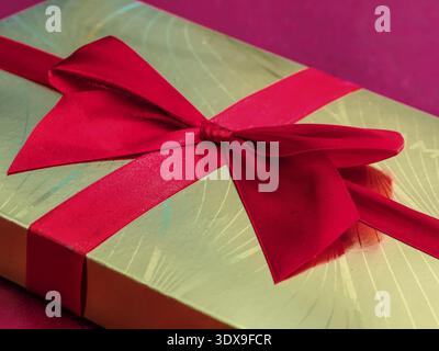 Nahaufnahme der goldenen Schokoladenbox mit rotem Band Stockfoto