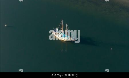 Aus der Vogelperspektive eines einsamen Segelboots, das auf dem ruhigen Wasser in der Nähe von Knysna Heads gleitet, eingerahmt von den stimmungsvollen Blau- und Grüntönen des umgebenden Ozeans, Knysna, W Stockfoto
