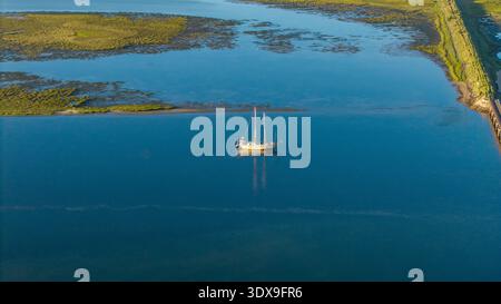 Aus der Vogelperspektive eines einsamen Segelboots, das auf den ruhigen Gewässern der Lagune unter dem riesigen Himmel gleitet, Knysna Heads in der Ferne, Knysna, Westkap, Süd-AFR Stockfoto