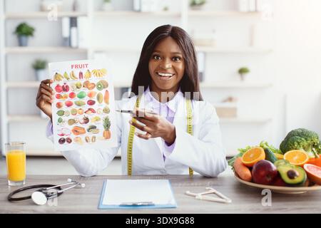 Gesundheitsexperte hält Fruchttabelle, während sie eine Ernährungssitzung in einer modernen Küche leitet Stockfoto