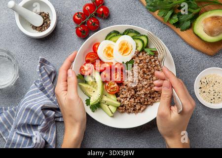 Frau essen gesunde vegane Mittagsschale mit Avocado, Ei, Gurke, Tomate und Buchweizen, Draufsicht Stockfoto