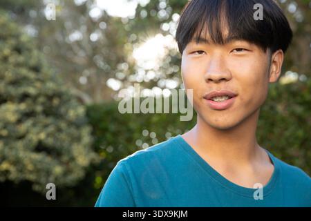 Asiatischer Mann, der draußen im üppigen Garten steht, mit blauem T-Shirt und Zahnspangen, Kopierraum. Natur, Grün, Ruhe, lässig, Lifestyle, VIBRANT, Wellness || Model veröffentlicht Stockfoto